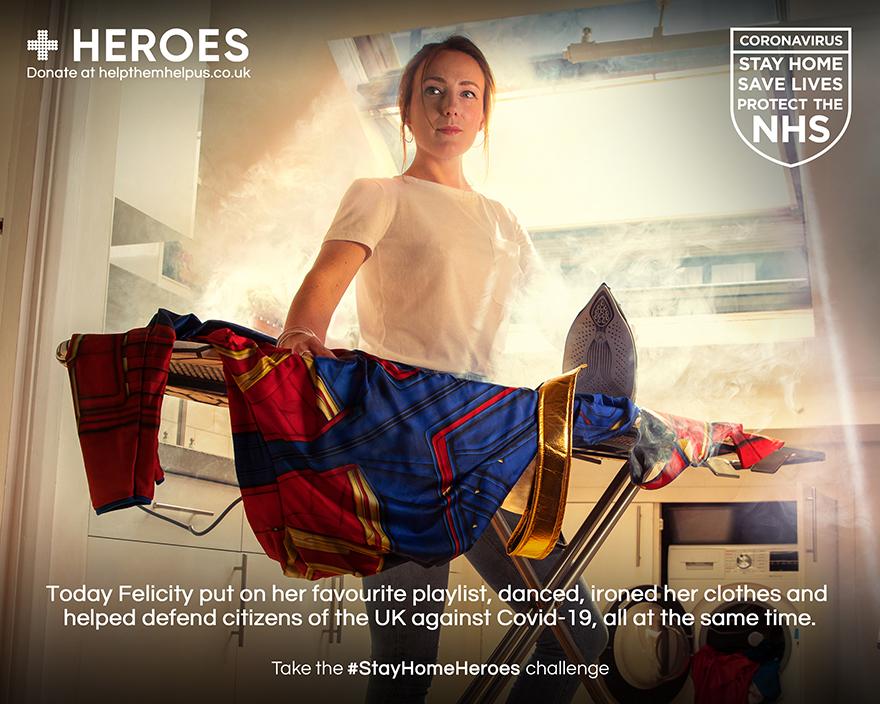 A woman in a superhero costume, standing in a kitchen, holding a superhero cape and a laundry basket, with a washing machine and a laundry dryer in the background.