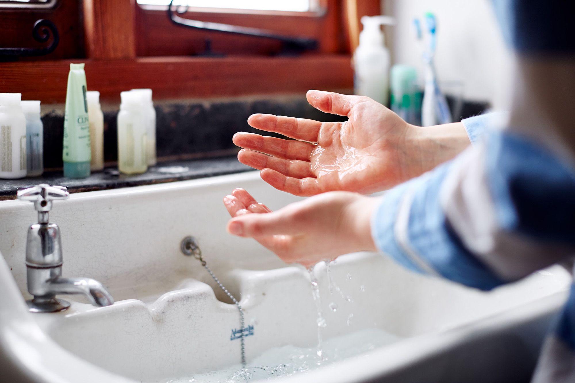 A person washing hands in a sink with soap and running water.