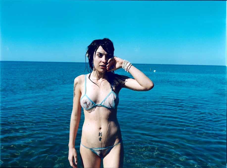A woman in a white bikini standing in the ocean, with the water and horizon visible in the background.