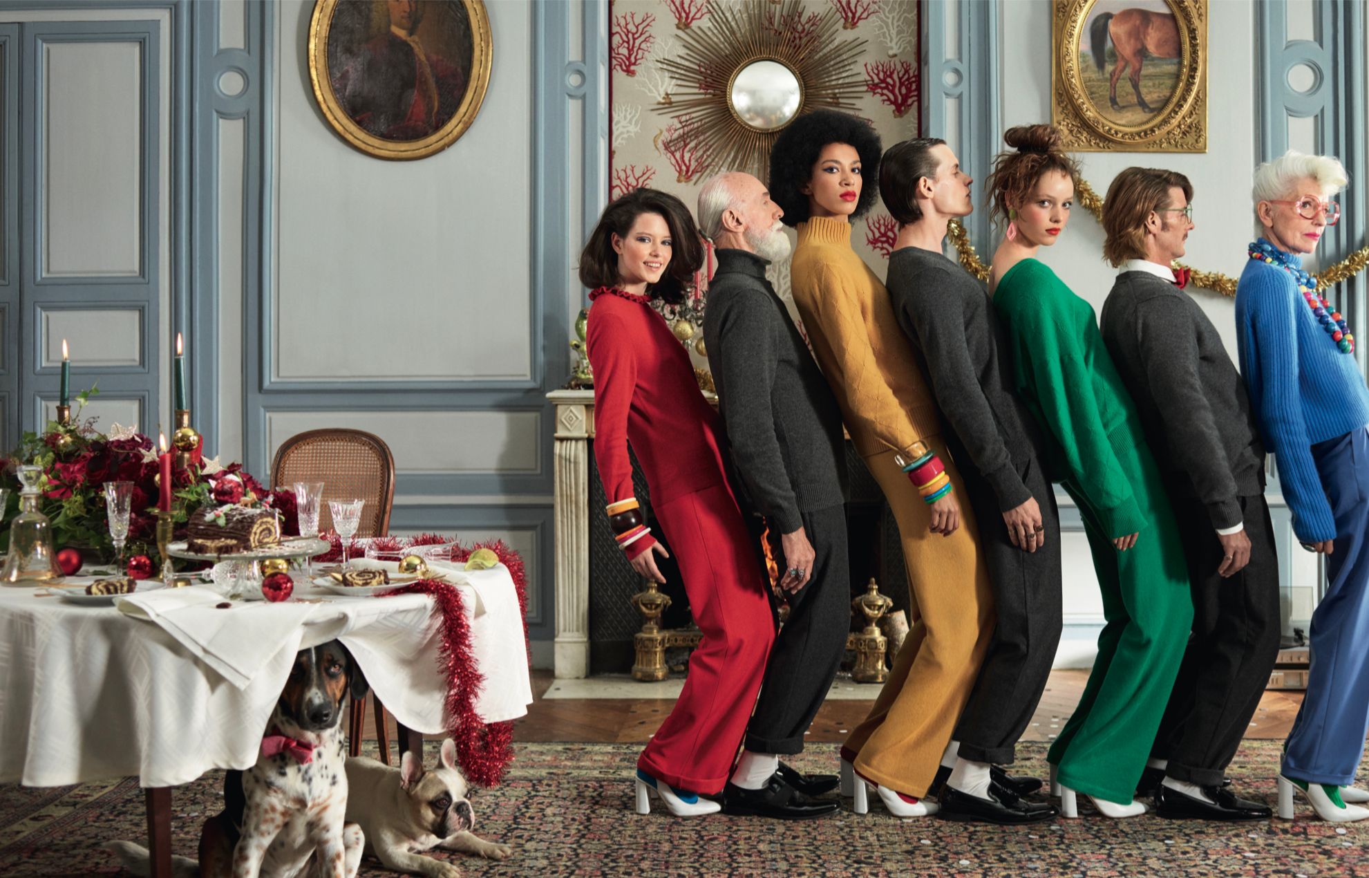 A group of people stand in a formal dining room with a table set for a meal and Christmas decorations.