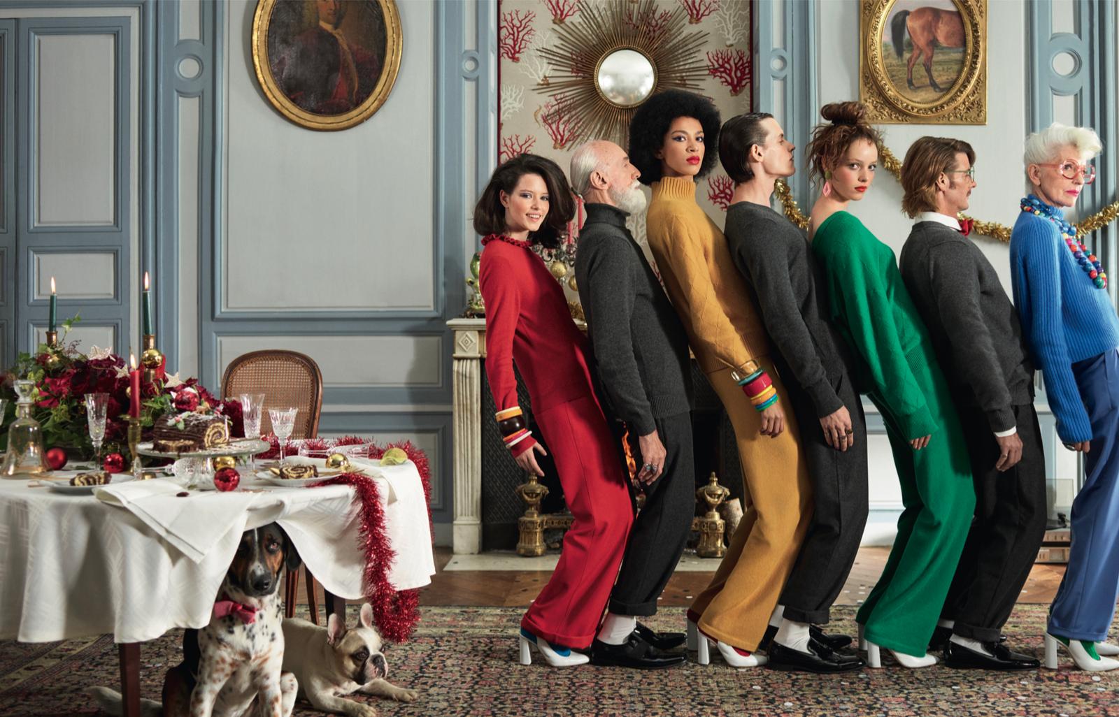 A group of people stand in a formal dining room with a table set for a meal and Christmas decorations.