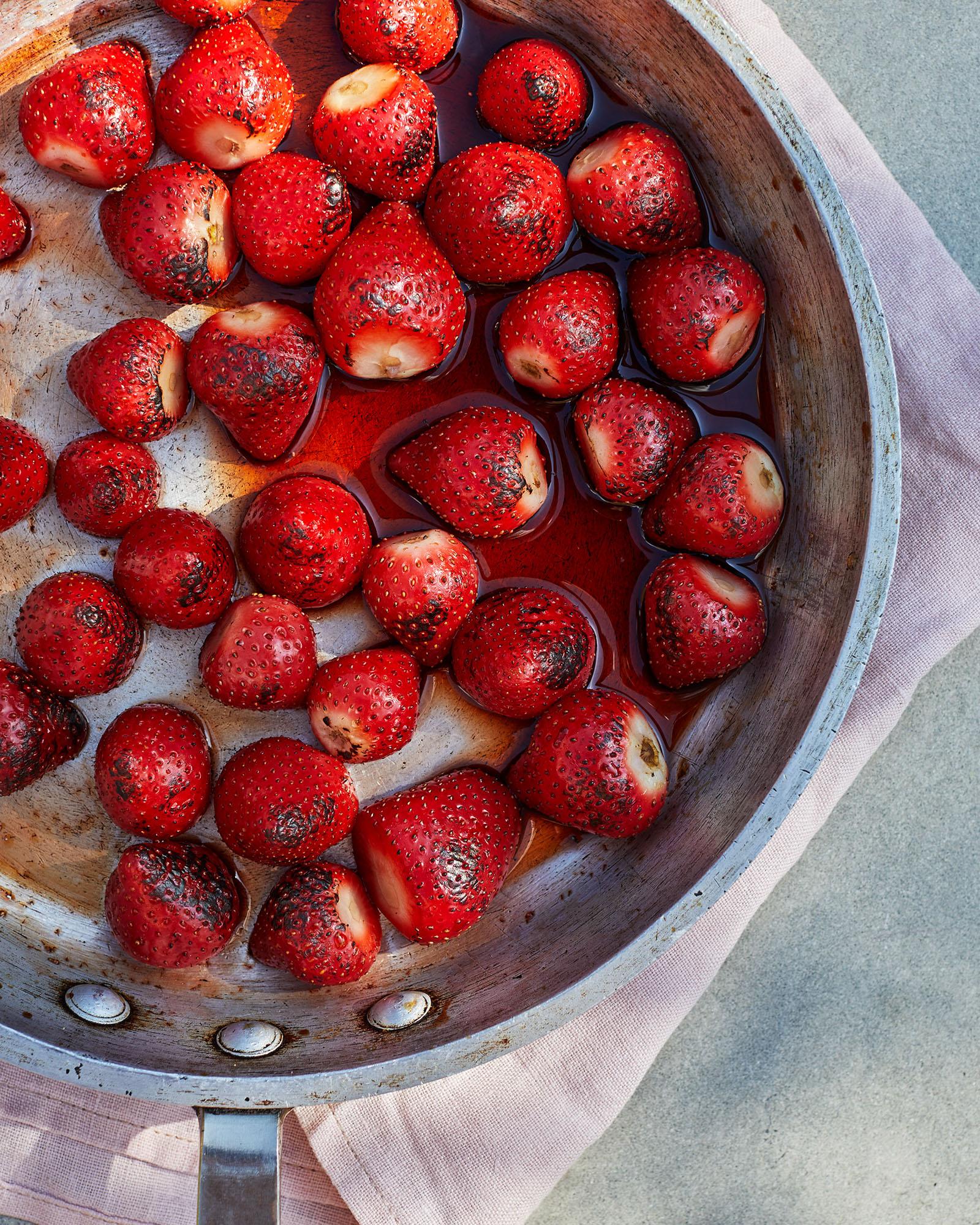 A large, shallow, metal pan filled with cooked, red, juicy strawberries in a sweet, red, syrupy liquid.