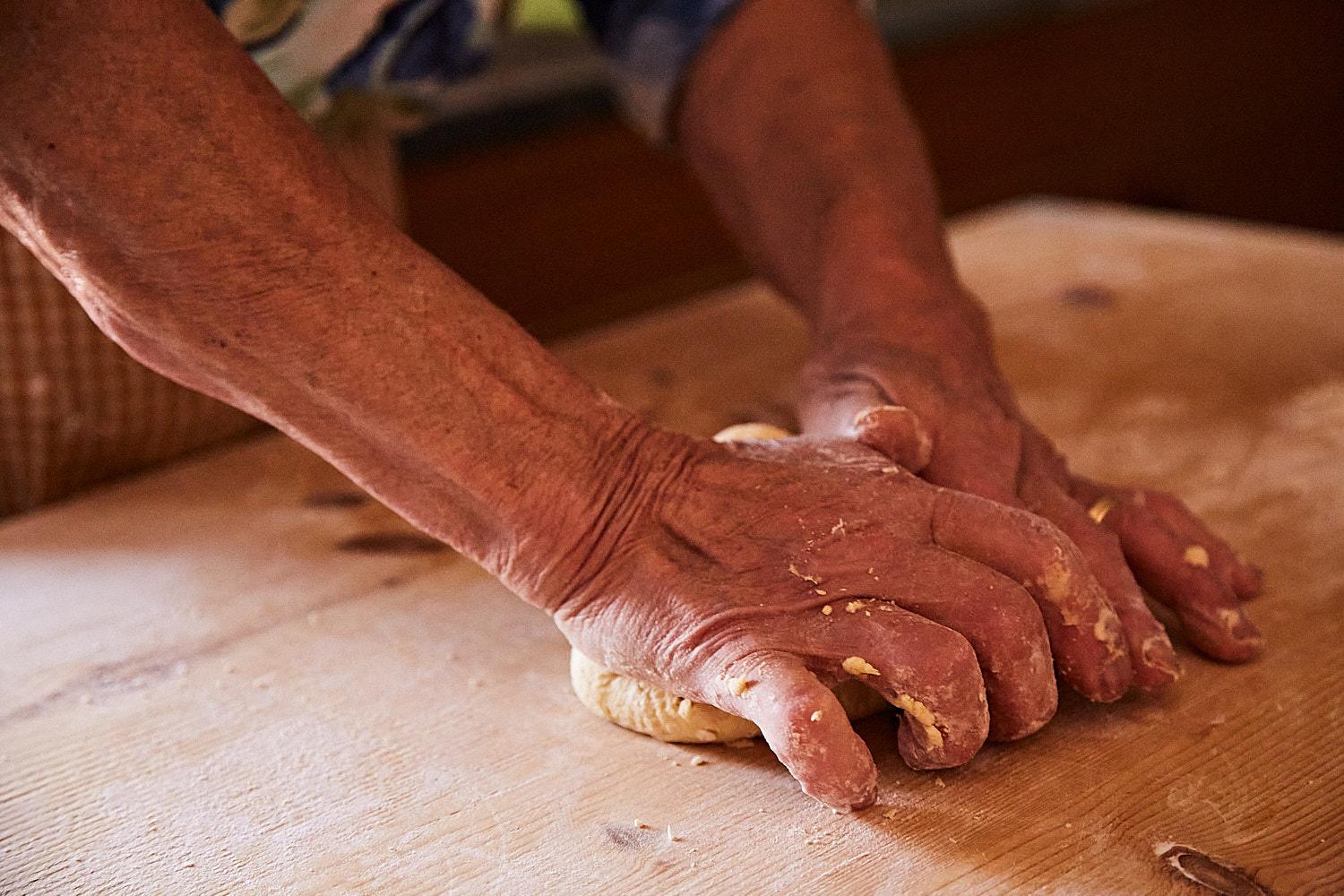 Hands knead dough on a wooden table.