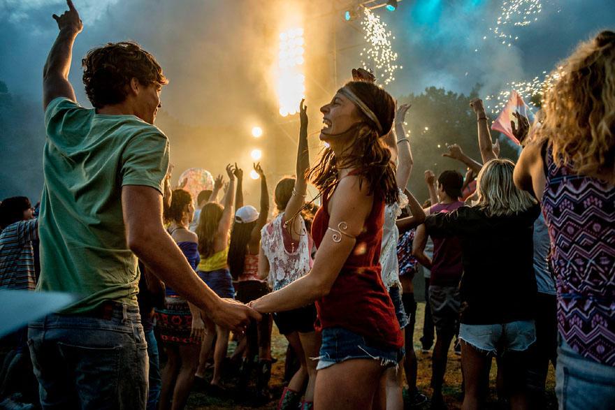 A crowd of people dancing and celebrating at a music festival, with a large stage and fireworks in the background.