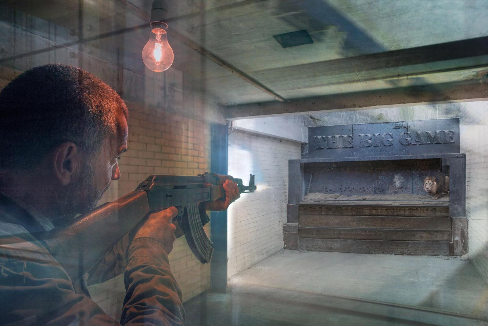 A man holds a rifle while aiming at a large metal game board featuring a lion’s head in an industrial room.