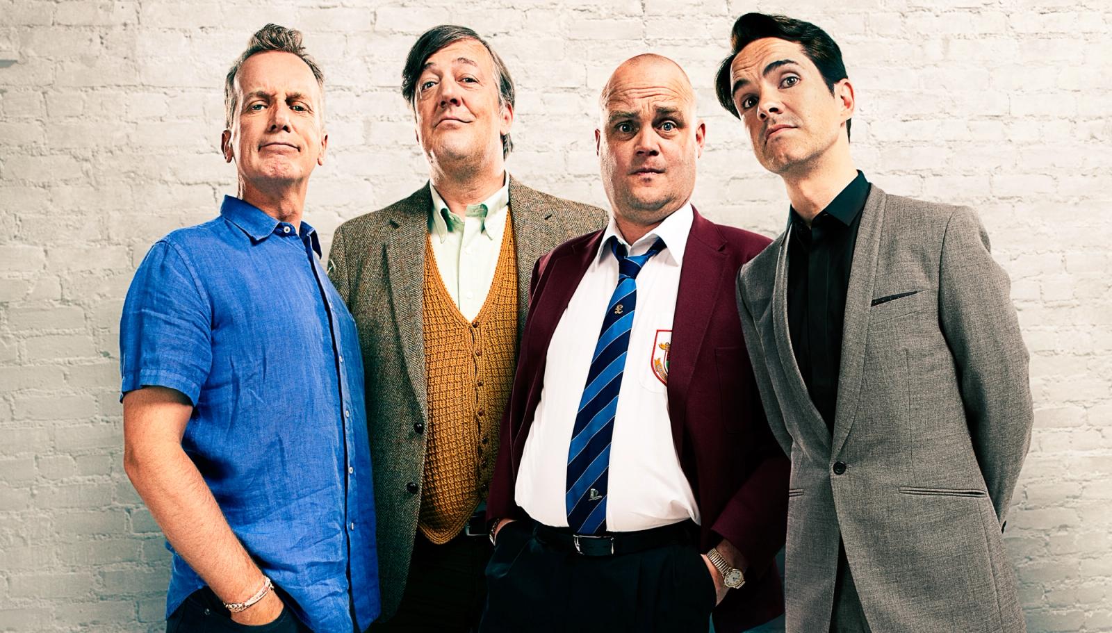 Three men in various outfits standing in front of a white brick wall, with one man in a blue shirt, one in a yellow sweater, and one in a red jacket.