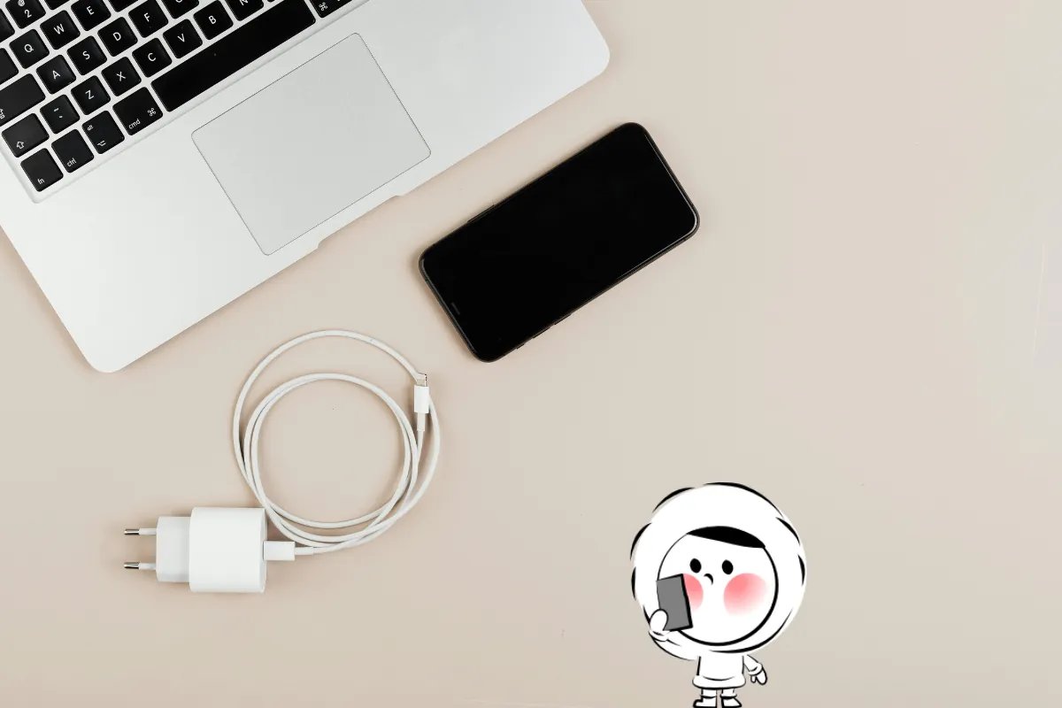 Laptop, smartphone, and travel charger on a beige desk representing how to charge devices safely abroad.