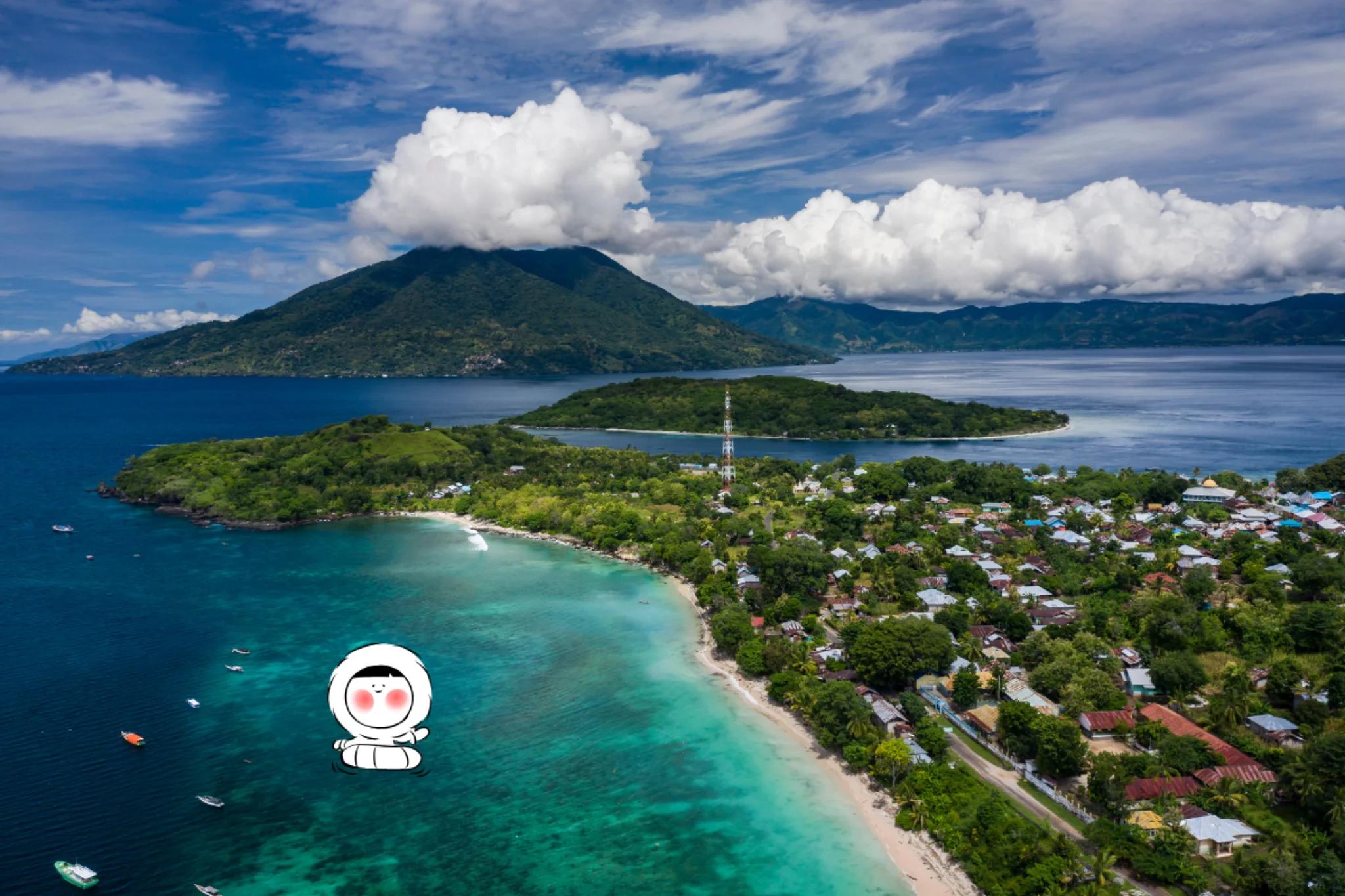 Aerial view of Alor Island with turquoise coastal waters, a sandy shoreline, lush green hills, and a seaside village beneath dramatic clouds.