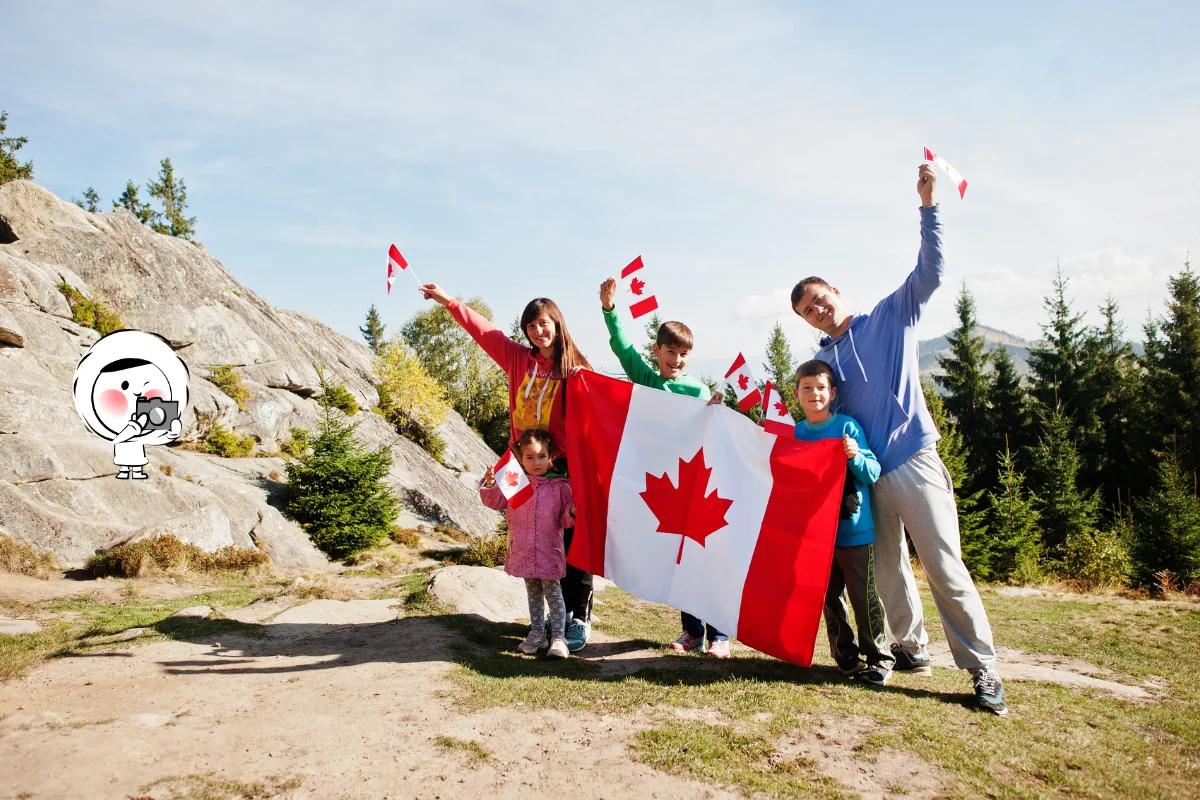 A family outdoors holding Canadian flags and a large Canada flag, celebrating Canada Day against a scenic mountain backdrop.