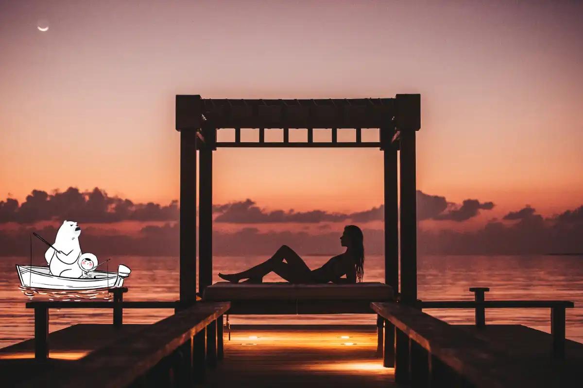 Silhouette of a woman relaxing on a deck over the ocean during sunset, with an Eskimo bear illustration fishing nearby.
