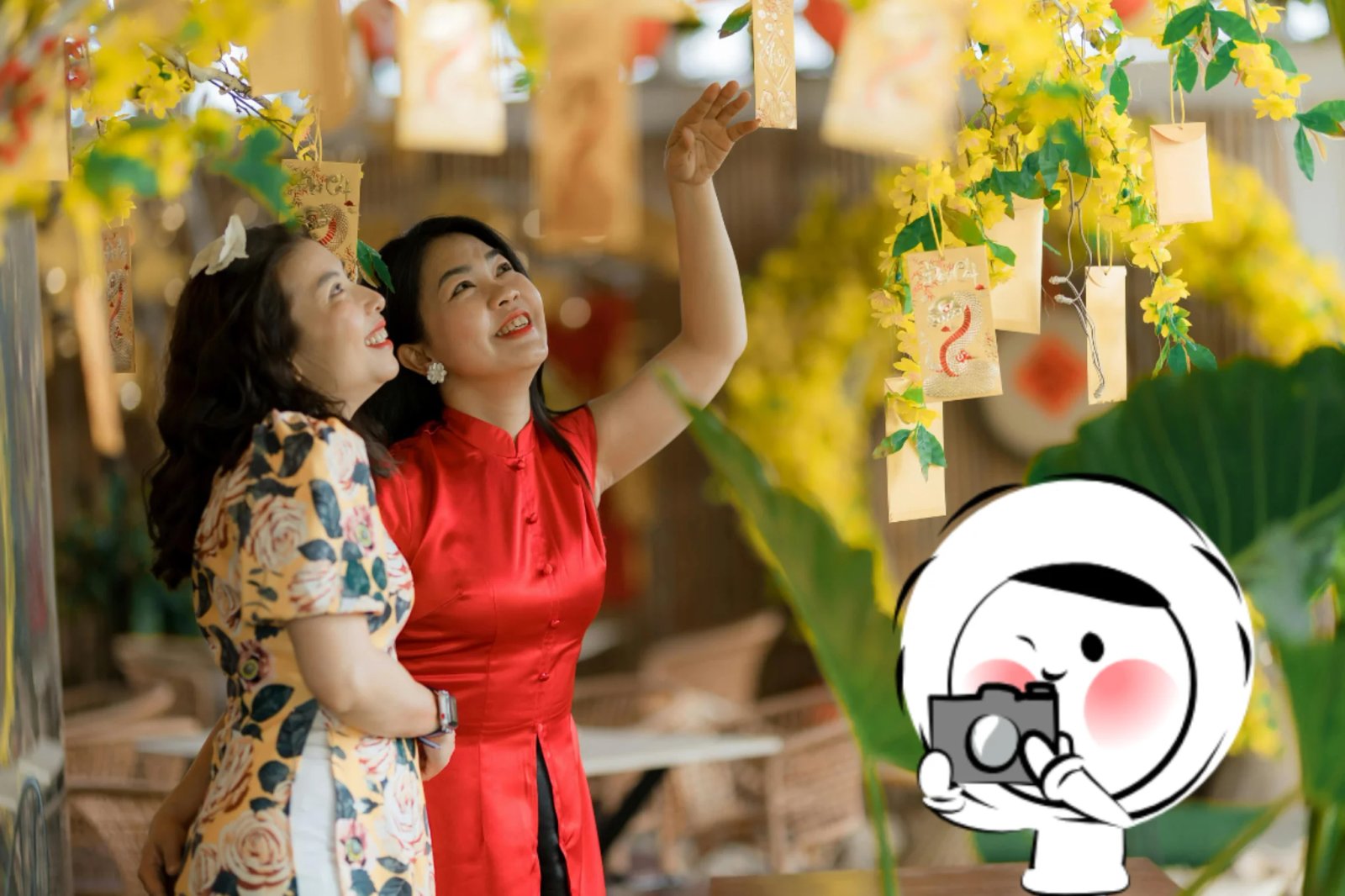 Two women celebrating Lunar New Year, smiling as they admire hanging decorative cards and yellow blossoms in a warmly lit festive setting.