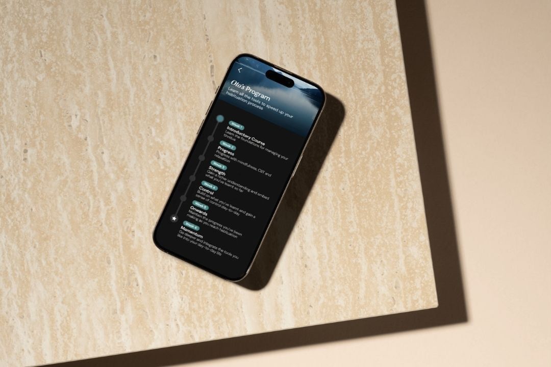 A phone on a stone table showing the Oto program, a week-by-week list of lessons