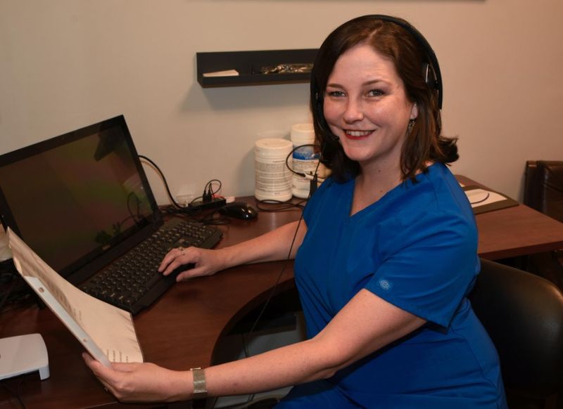An audiologist wearing a headset smiling at her desk