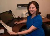 An audiologist wearing a headset smiling at her desk