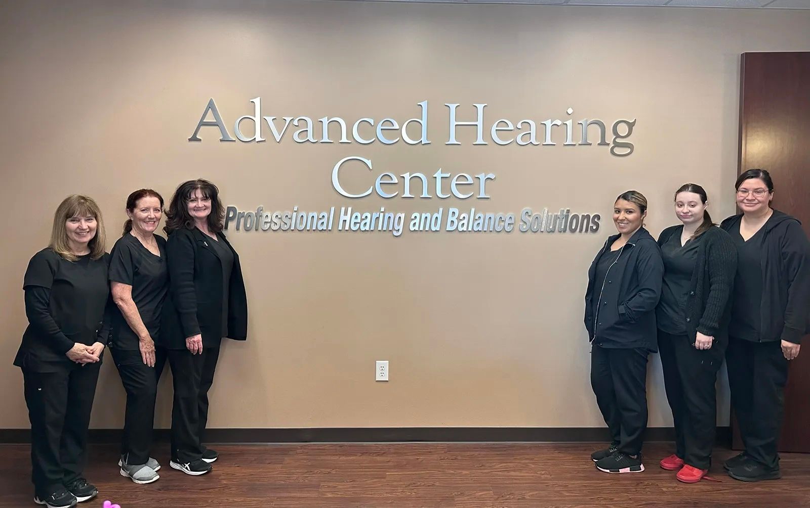 Seven members of the Advanced Hearing Center team in front of the practice sign