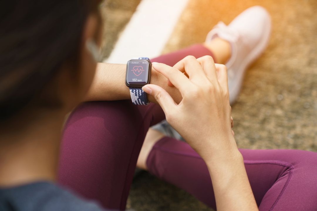 A person sitting on the floor checking a heart rate reading on a smartwatch