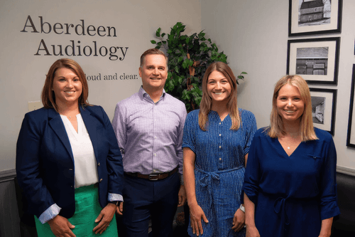 Four members of the Aberdeen Audiology team in front of the practice logo