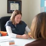 An audiologist smiling as she talks with a patient across a desk