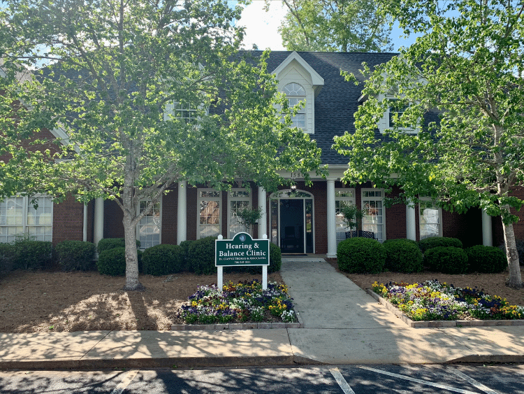 The brick Hearing & Balance Clinic office in Watkinsville with a green sign and flower beds out front