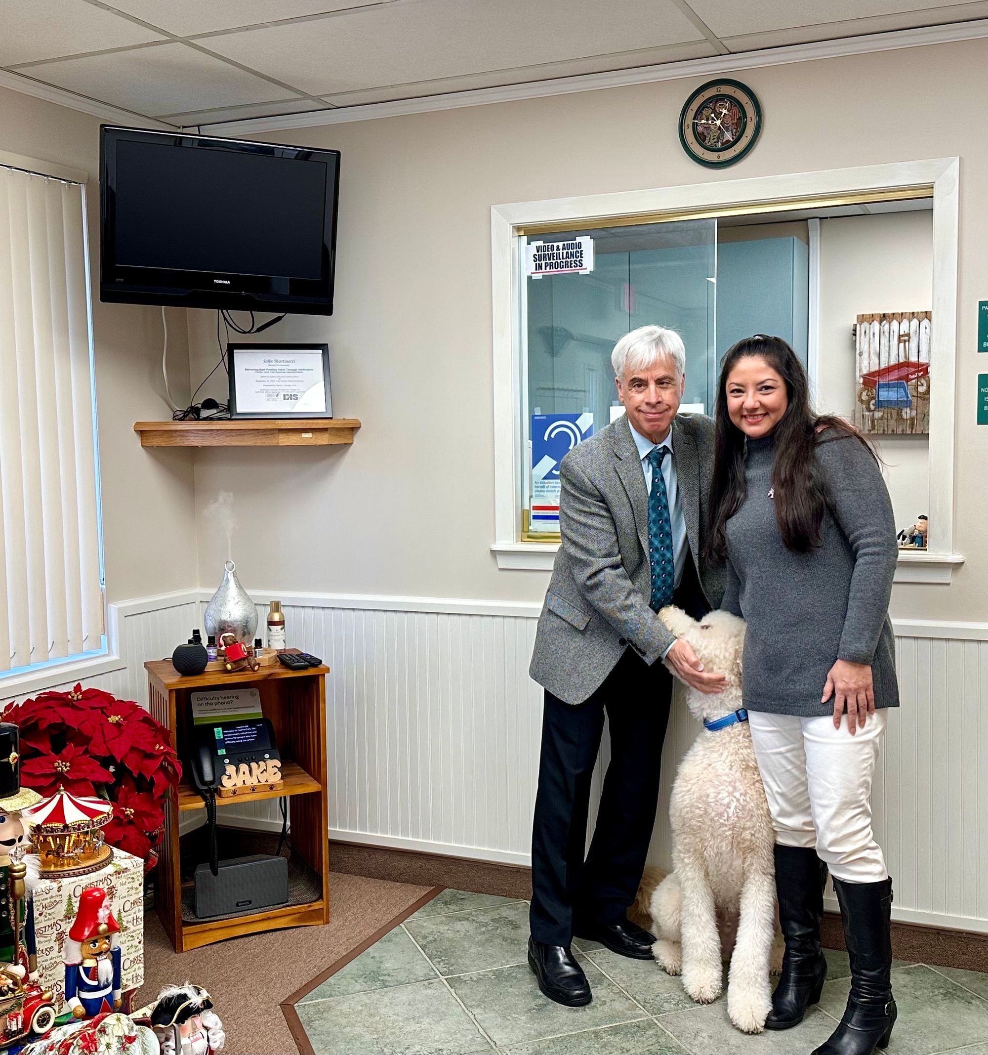 Dr. John Martinetti and a Port Jefferson Hearing team member with a white poodle in the waiting room