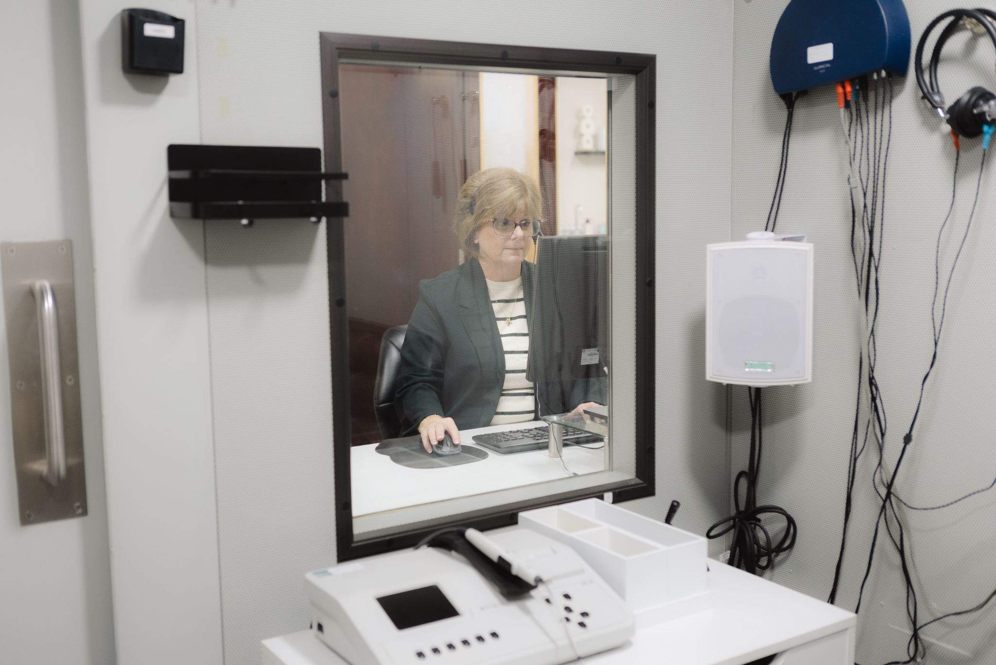 A clinician seen through the window of a hearing test booth