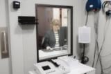 A clinician seen through the window of a hearing test booth