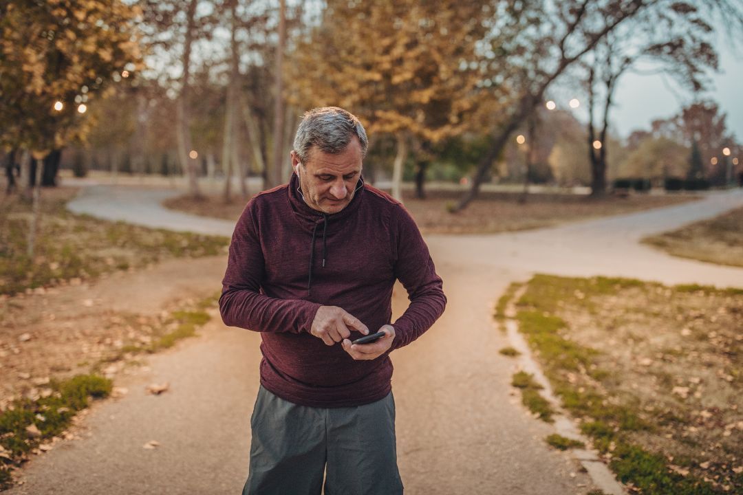 A man on a park path in autumn looking down at his phone