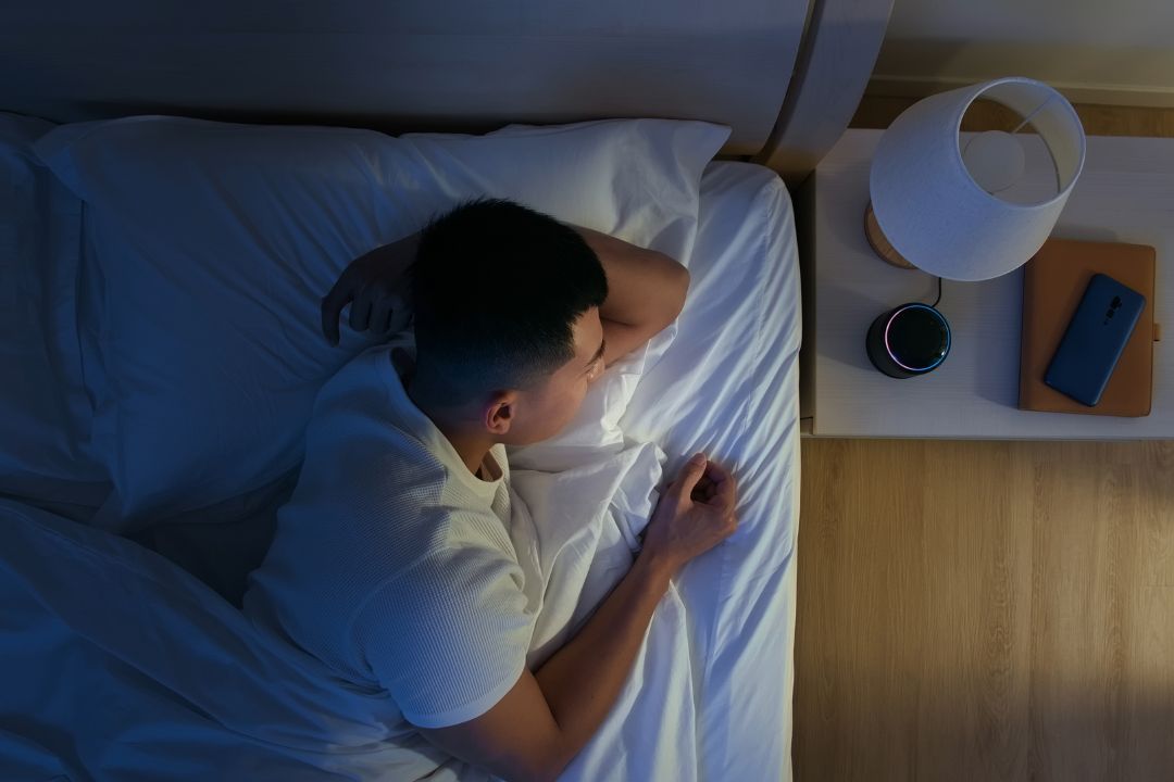 A man asleep in bed at night with a small speaker on the bedside table