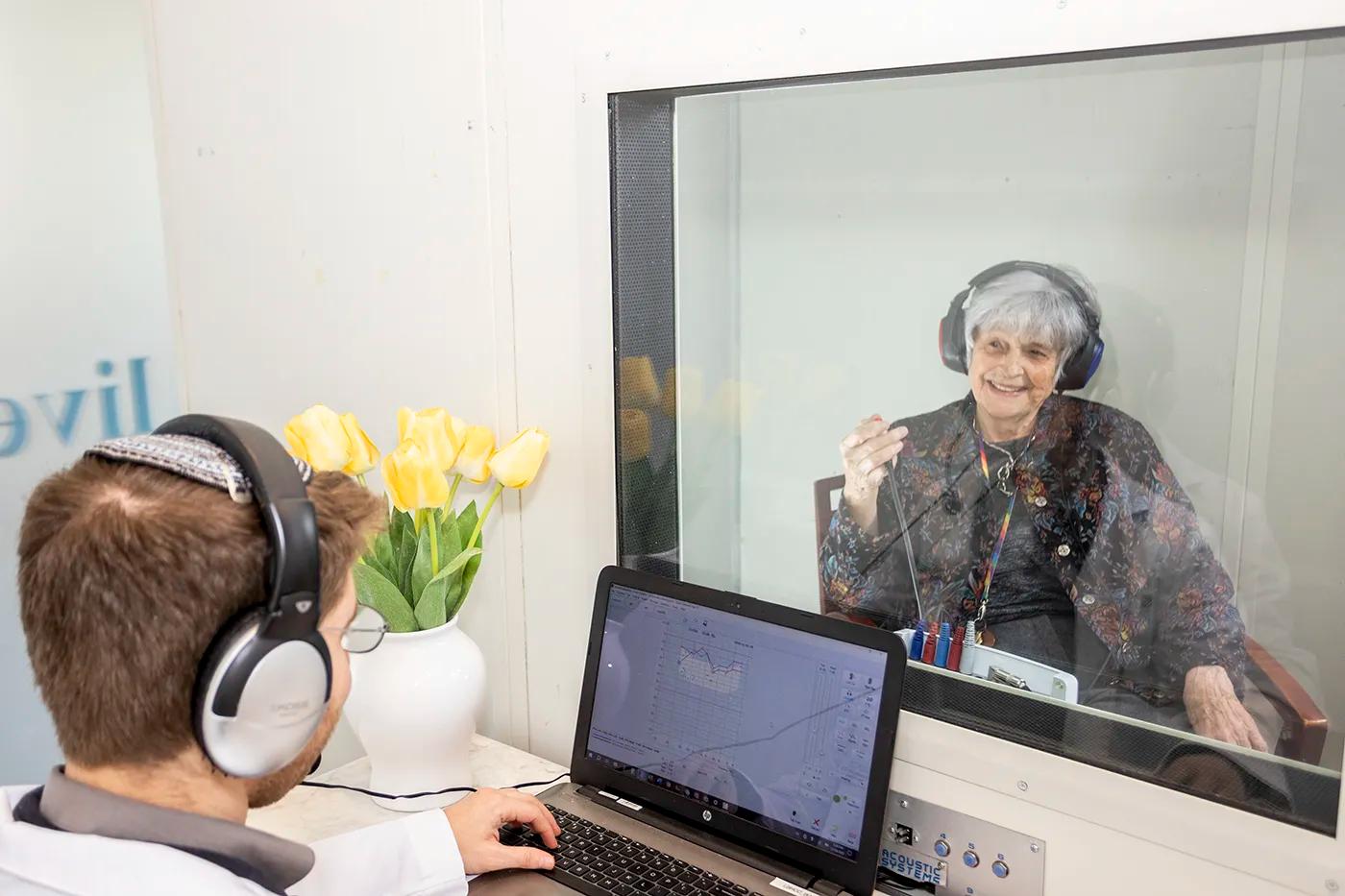 A Live Better Hearing + Balance audiologist running a hearing test with a patient in the sound booth