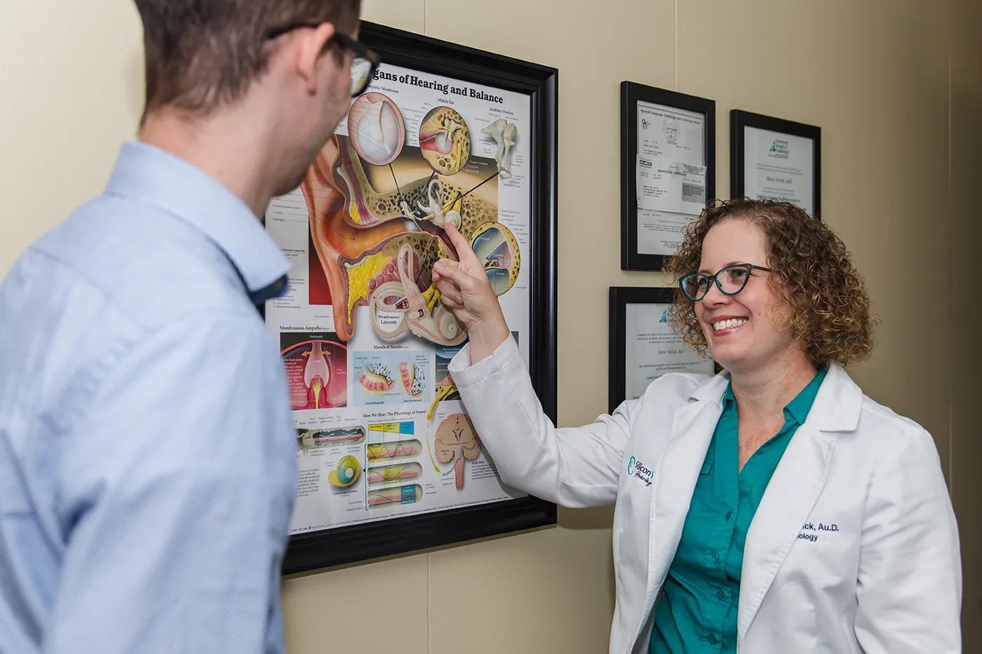 An audiologist in a white coat pointing to a chart of the ear while talking with a patient