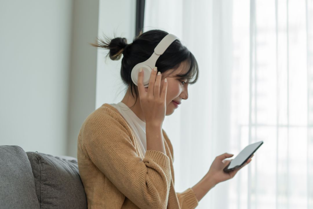 A woman on a sofa wearing headphones and looking at her phone
