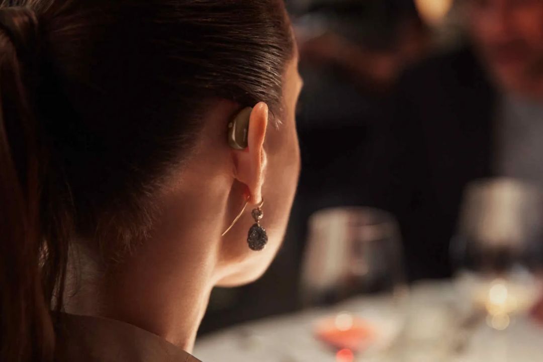 A woman wearing a small behind-the-ear hearing aid at a dinner table