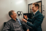 An audiologist fitting headphones on a smiling patient in a hearing test room