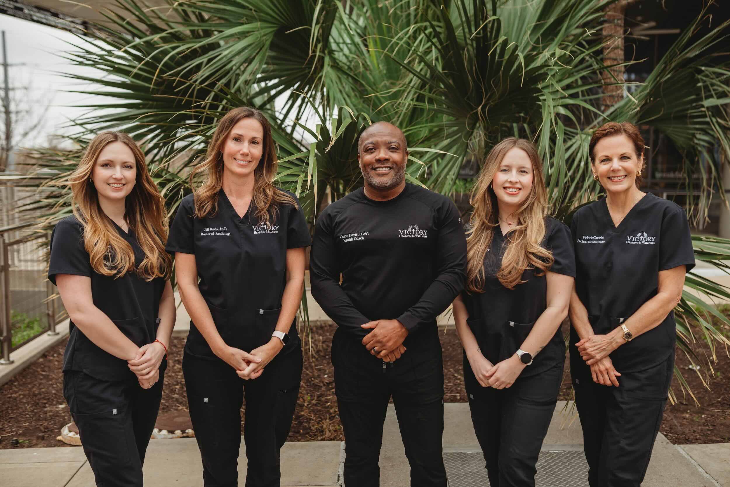 The Victory Hearing & Balance team in matching black scrubs standing in front of palm plants