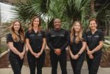The Victory Hearing & Balance team in matching black scrubs standing in front of palm plants