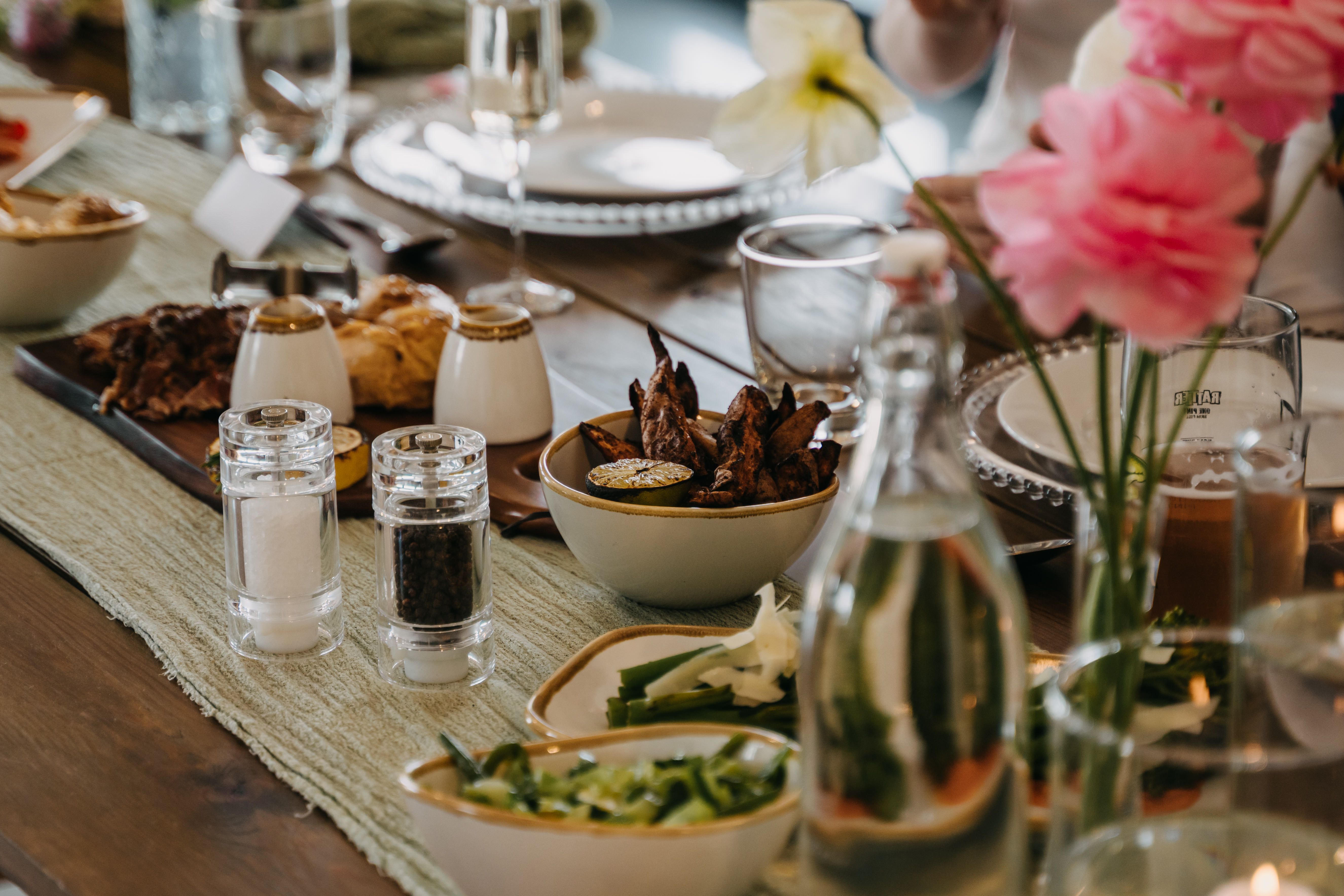 Dinner table set with shared dishes, drinks, and flowers for guests
