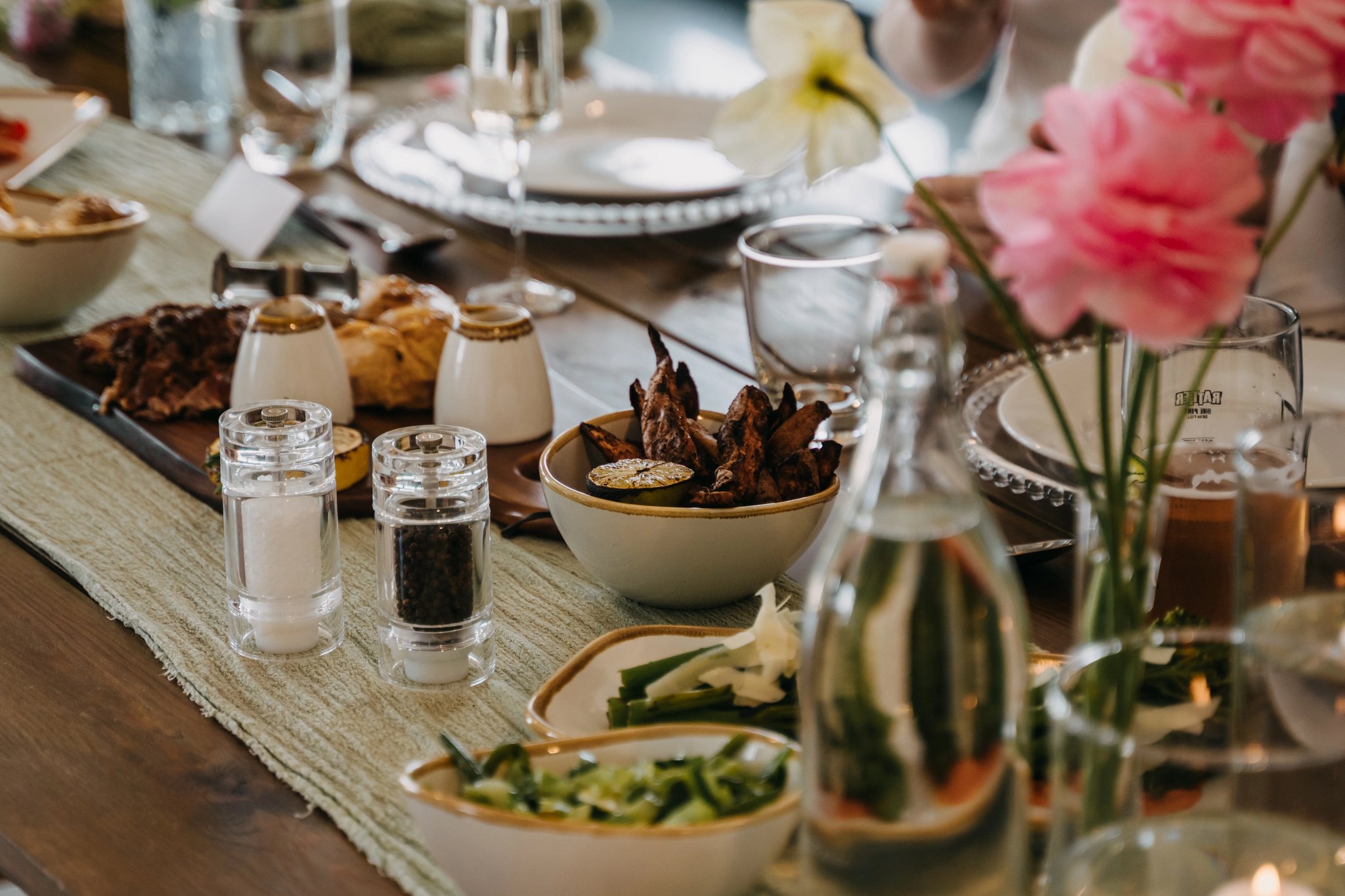 Dinner table set with shared dishes, drinks, and flowers for guests