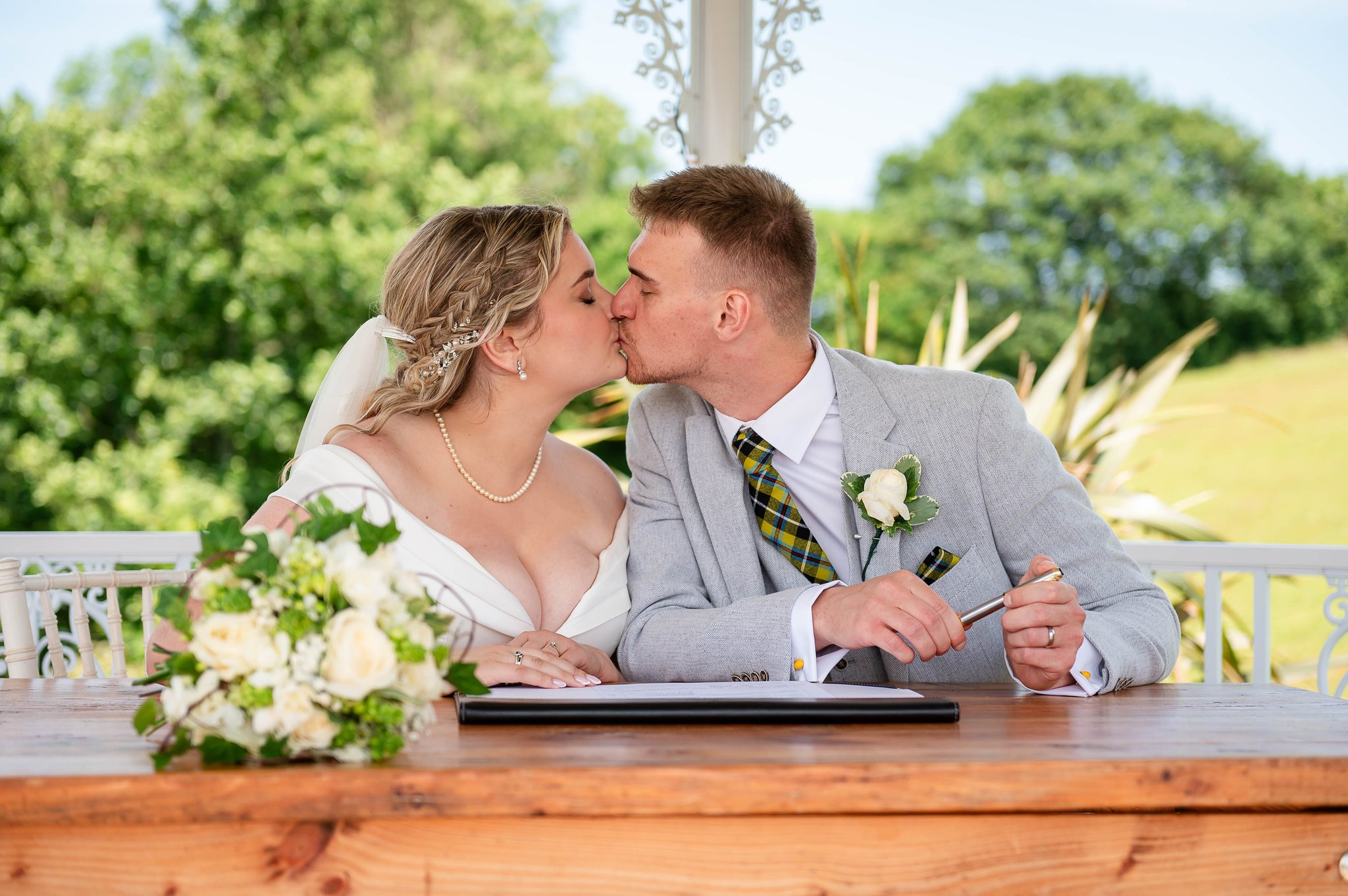 Bride and groom kiss while signing their wedding register outdoors