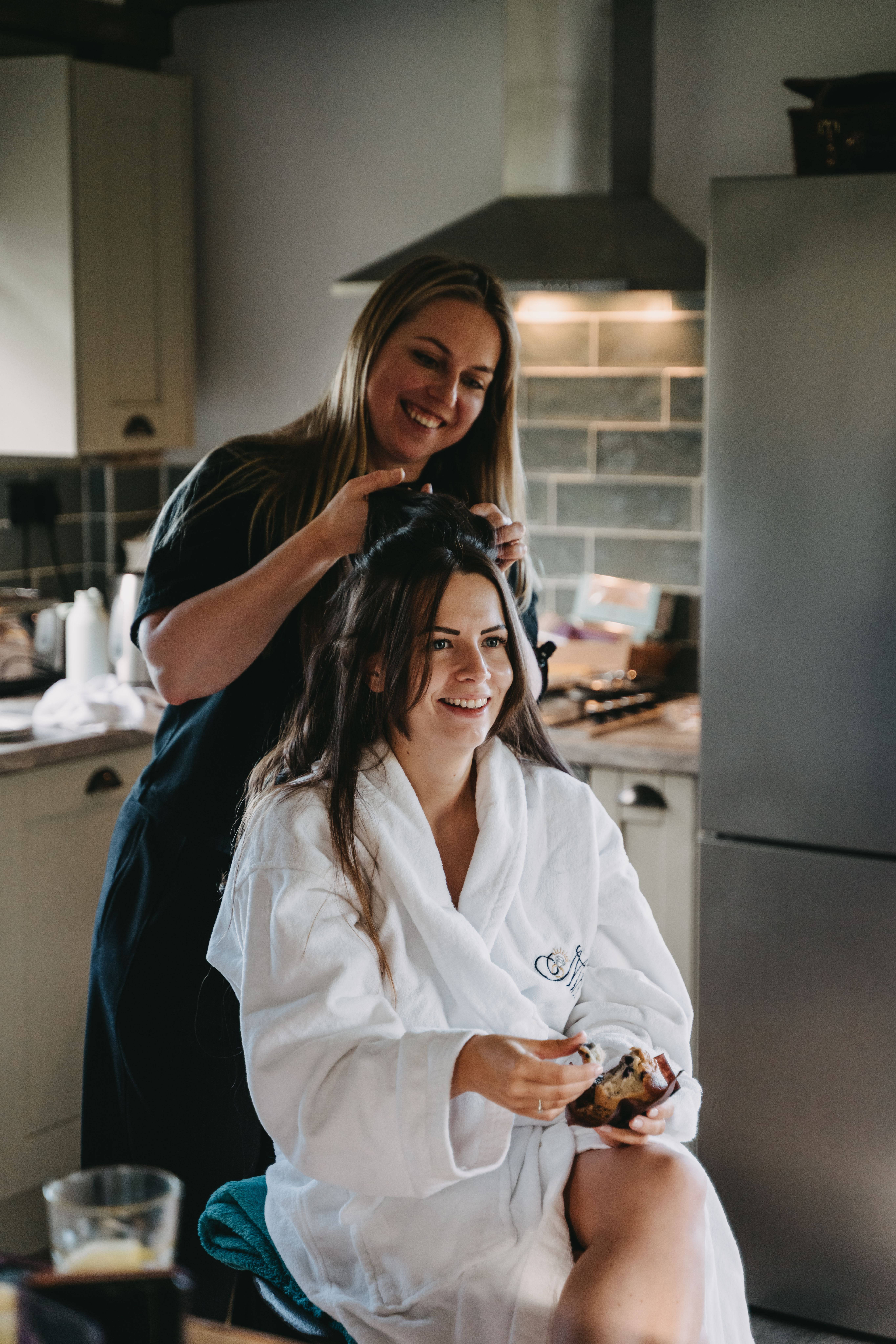 Bride in robe getting her hair styled while eating a pastry