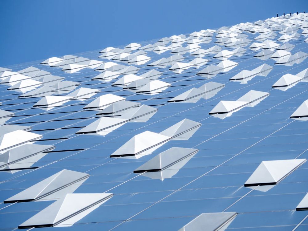 White faceted panels projecting from a blue glass facade viewed from below