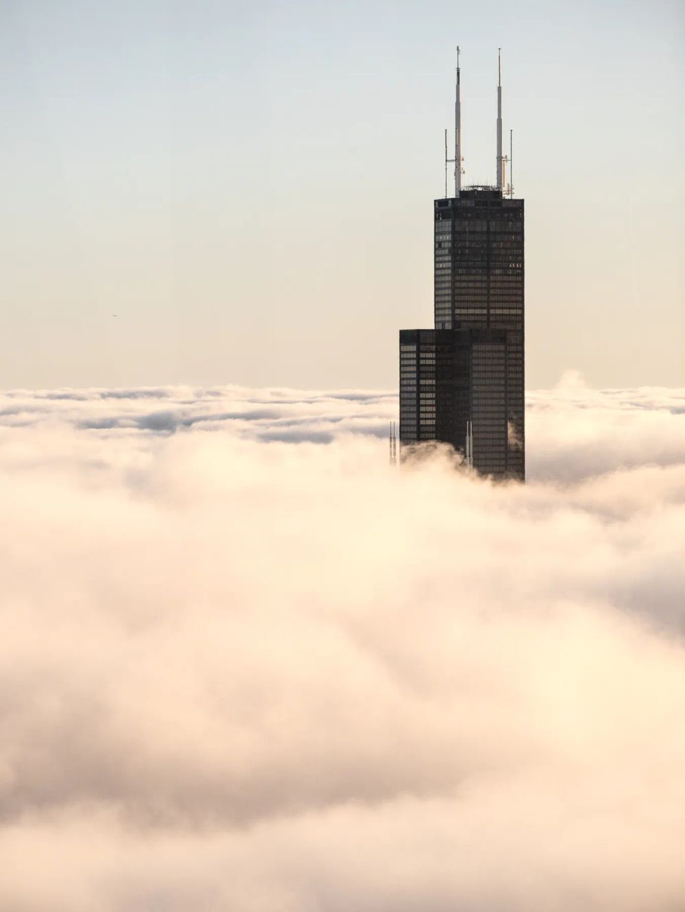 A dark twin-antenna tower emerging above a blanket of sunlit fog