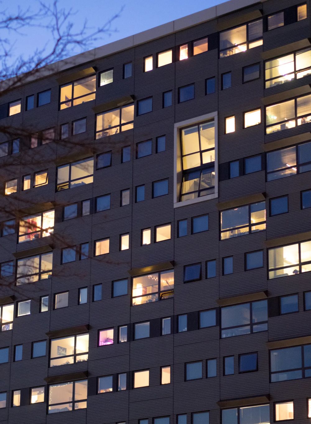 Warmly lit apartment windows scattered across a dark facade at dusk