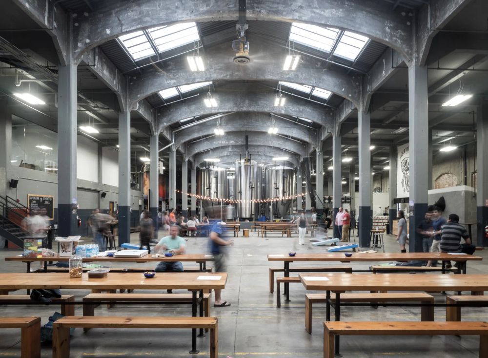 People moving among tables beneath the rooflights and columns of an industrial hall