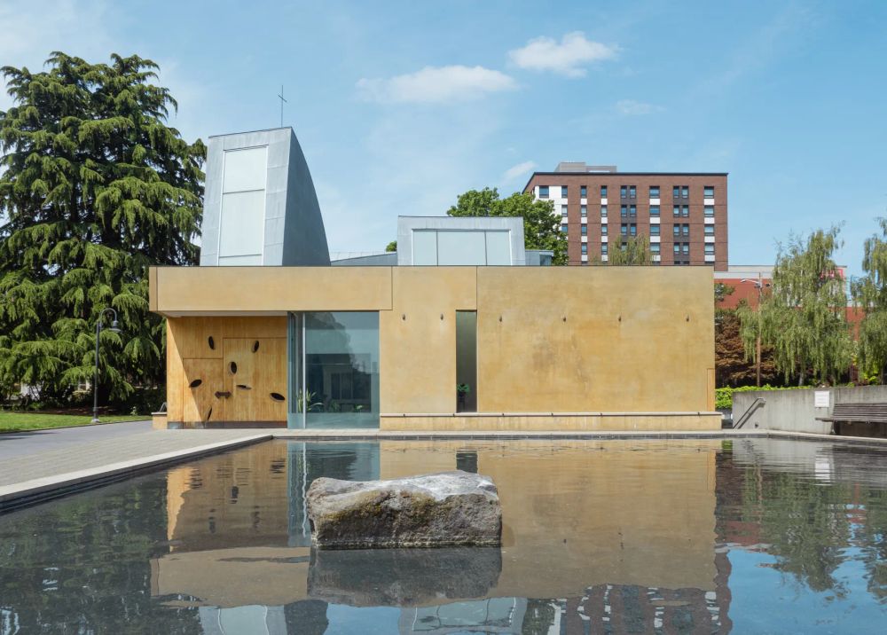 A low ochre building beside a reflecting pool with a stone in the water