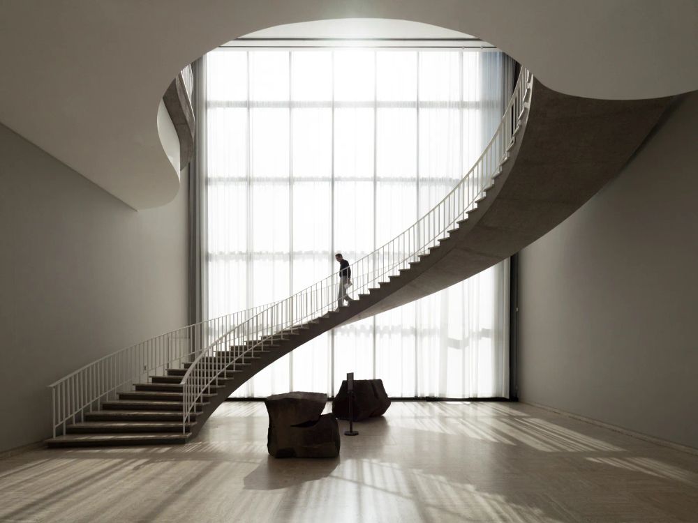 A person on a sweeping stair silhouetted against a tall sunlit window