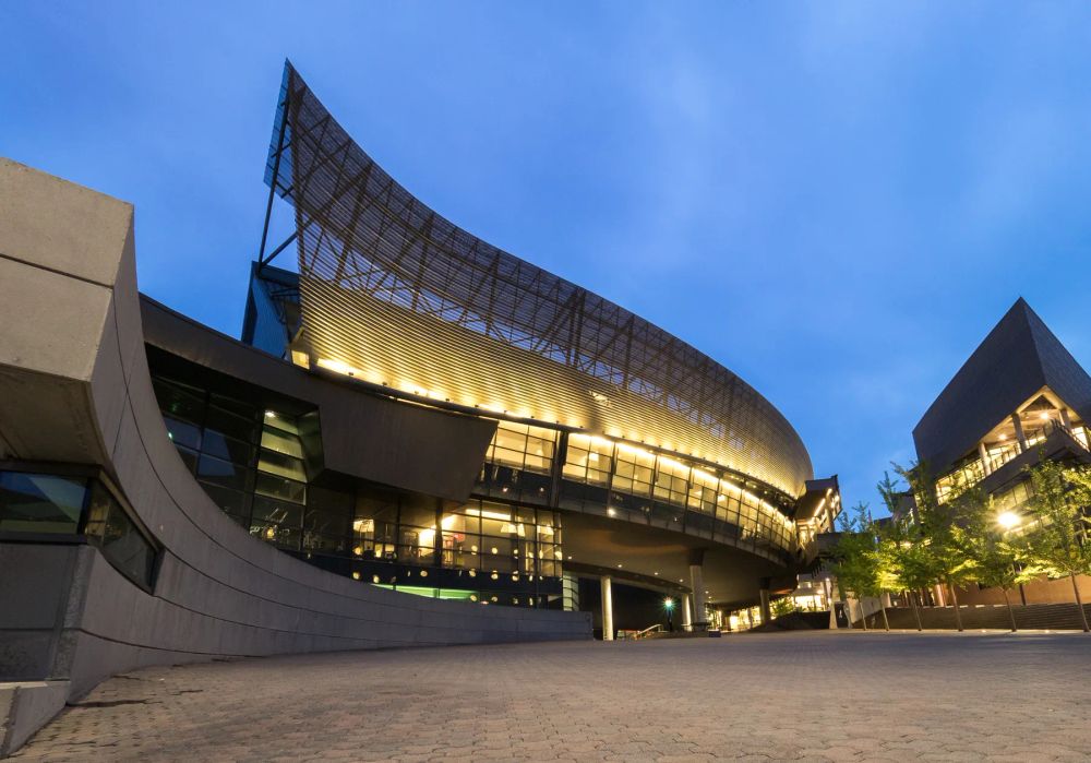 An angular cultural building glowing against a blue evening sky