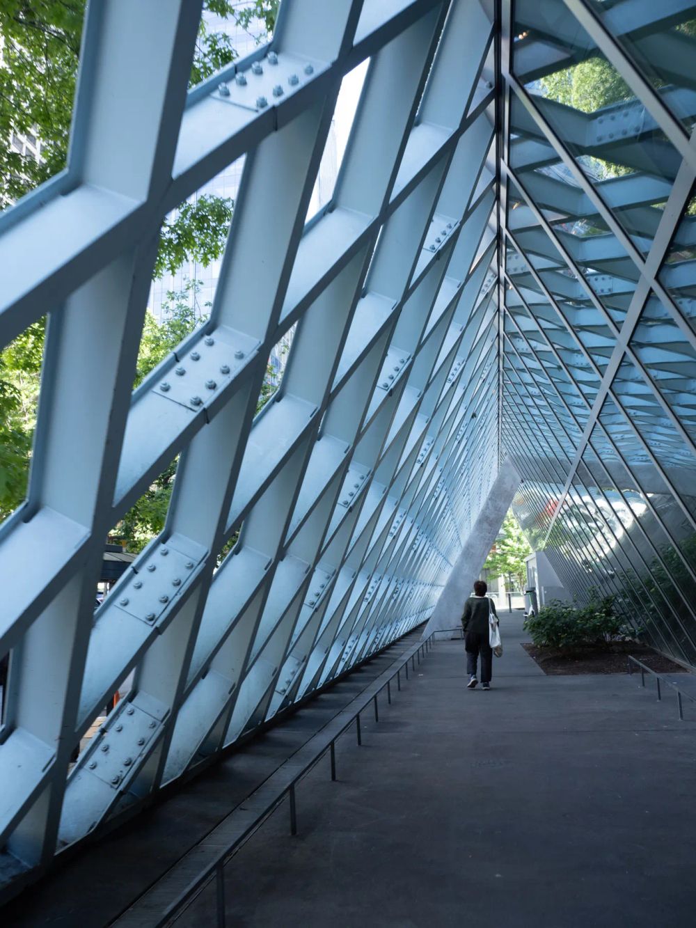 A lone person walking beside a sloping diamond-patterned glass wall