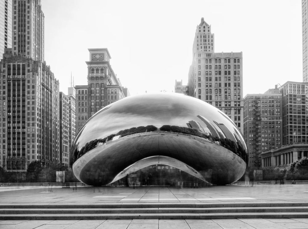 A reflective oval sculpture framed by city towers in black and white