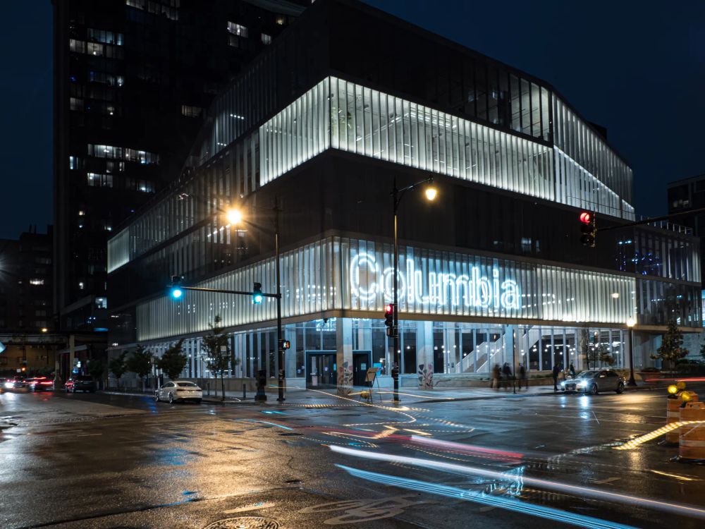 Vehicle light trails on wet paving beside an illuminated glass building