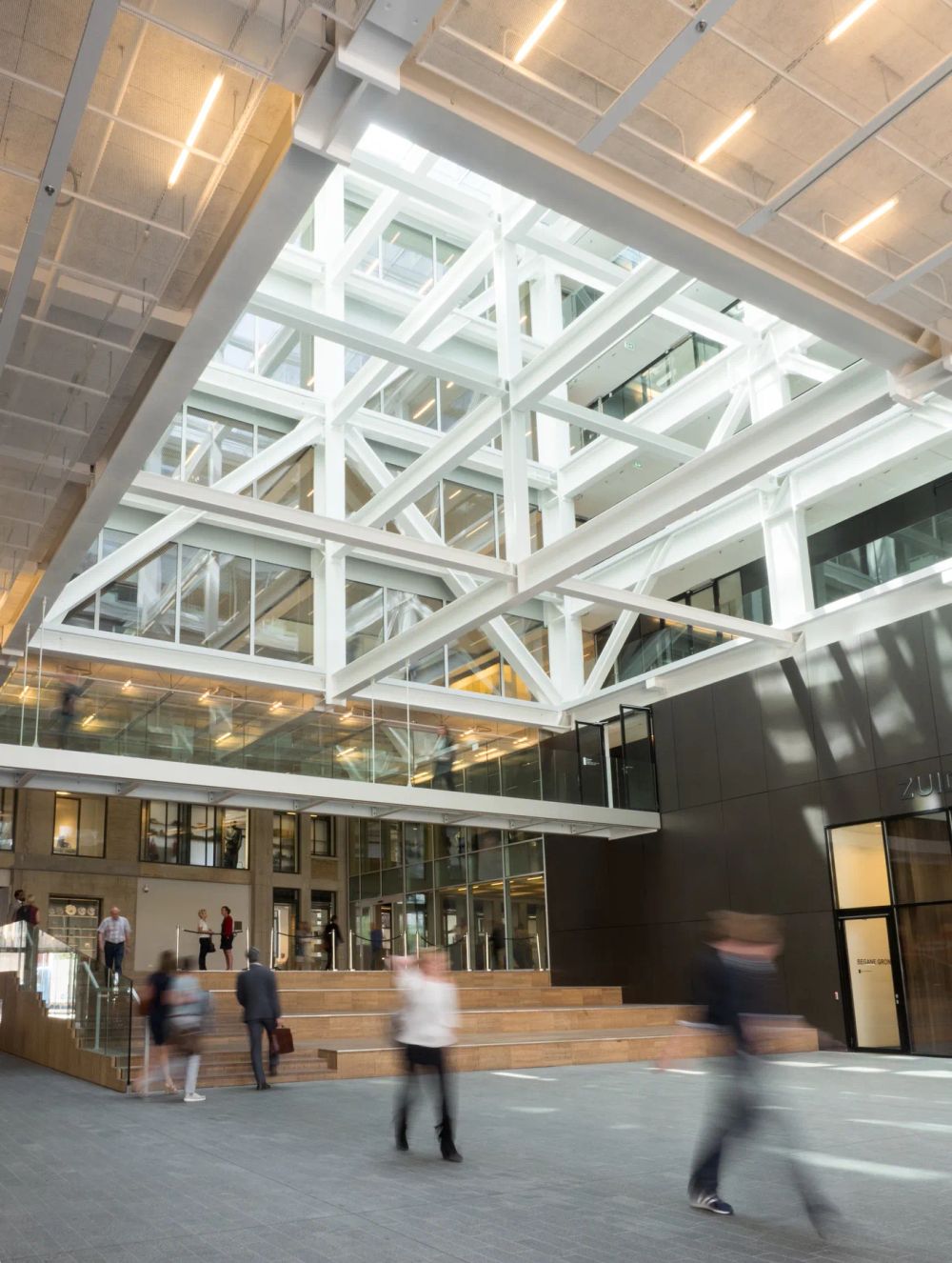 Blurred visitors beneath white structural trusses in a bright atrium